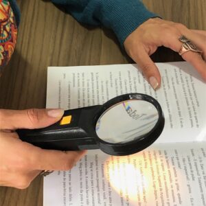 lupa de mão 65mm 4x com luz sendo usada para ler um livro