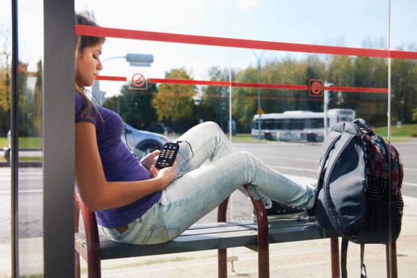 Jovem no ponto de ônibus com seu leitor digital Victor Reader Stream